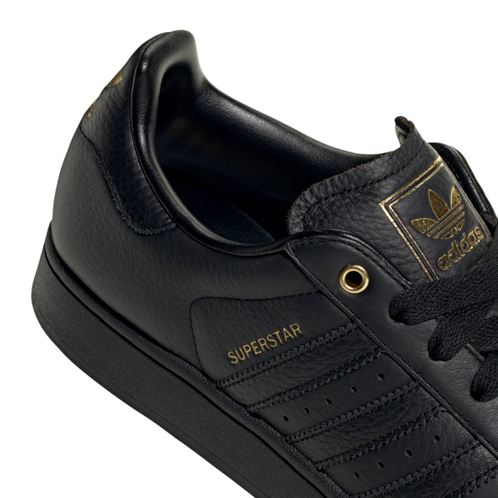 Men's black leather low-top sneakers, Superstar logo patch and gold lace eyelet.
