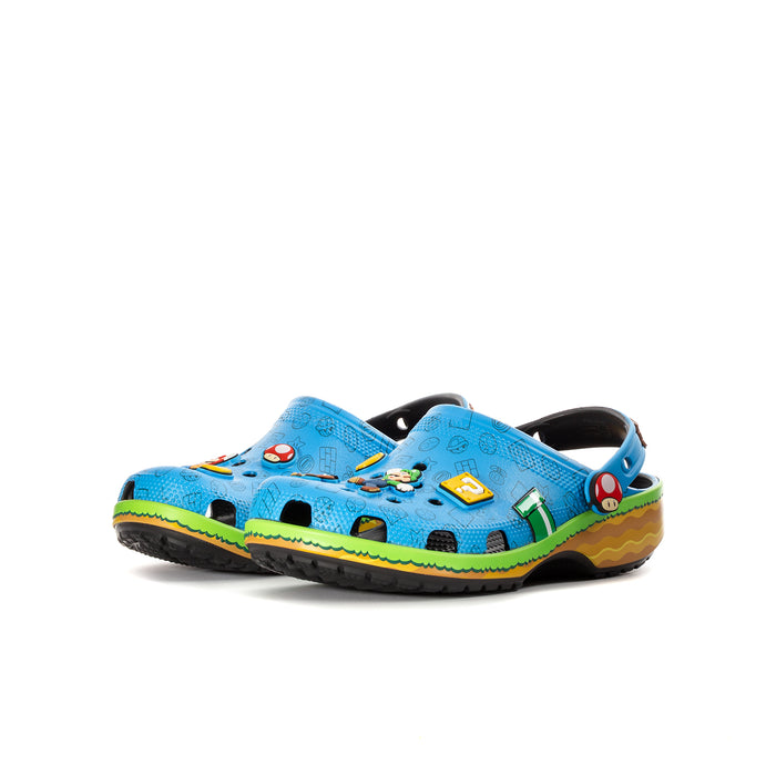 Youth blue clog with black lining, green/yellow wavy sole, cartoon game icons.