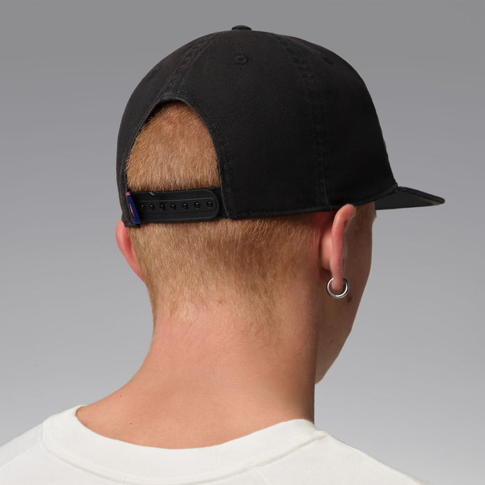 Black snapback cap with adjustable back strap, logo not visible, worn from behind.