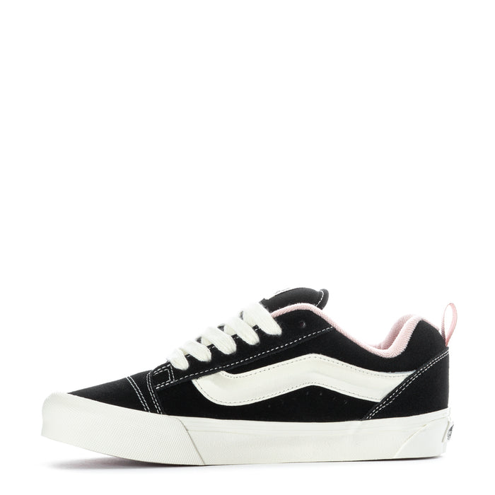 Black and white low-top sneakers with pink collar lining, front quarter view.