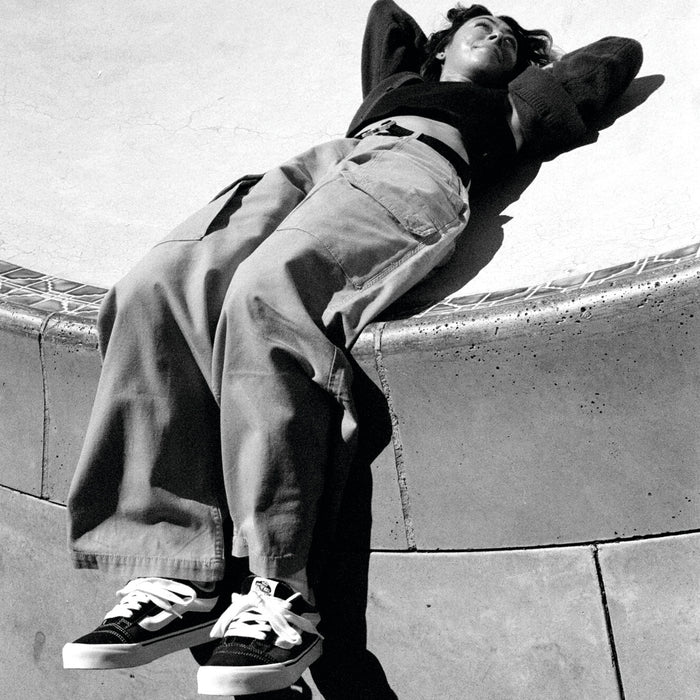 Low-top black and white sneakers with white laces, worn and resting on pavement