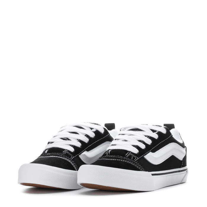 Pair of black youth lace-up sneakers with white wavy side stripe and thick white sole.