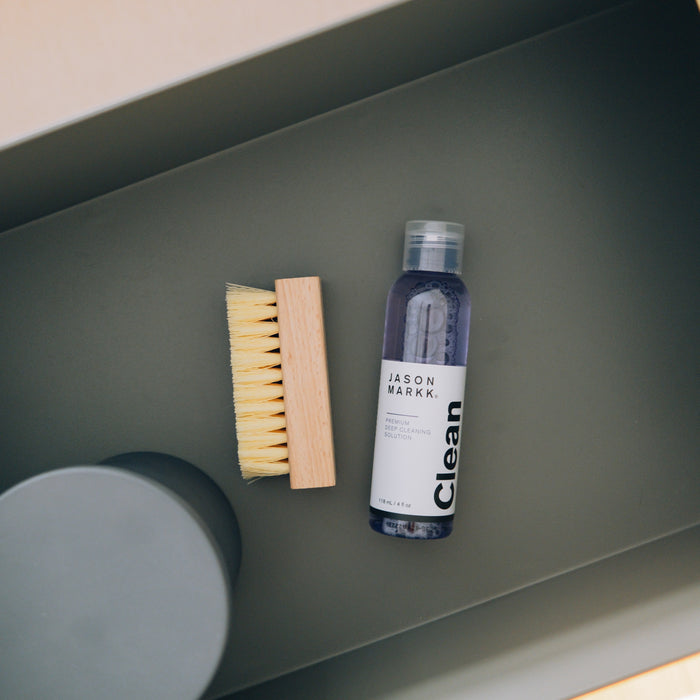 Shoe cleaner bottle with bristle brush and foam cleaning pad on shelf.