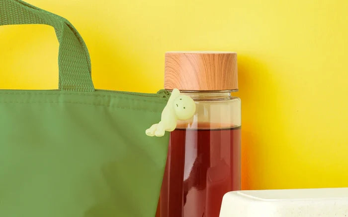 Smiski ZipperBites toy keychain on a bottle of liquid, designed to hide in small spaces and glow in the dark.