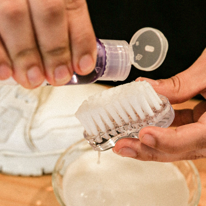 Hands scrubbing a white shoe with the oval brush and deep cleaning solution