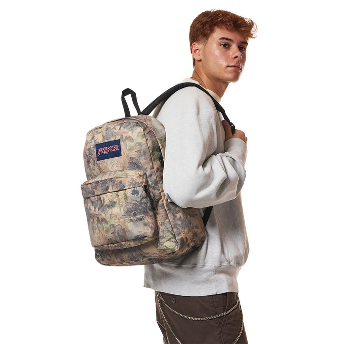 JanSport Superbreak Plus camo backpack worn by a person, side view with top handle