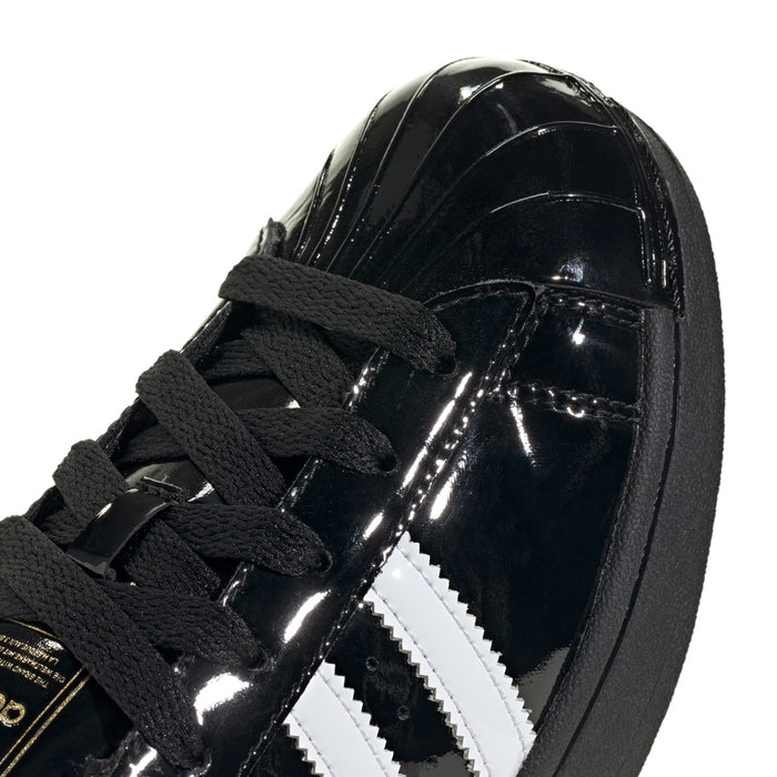 Women’s black patent leather sneaker close-up with white stripe detail and black laces