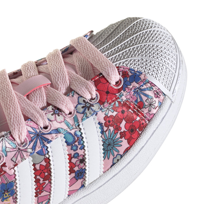 Youth sneaker close-up, pink laces over floral print with white three stripes.