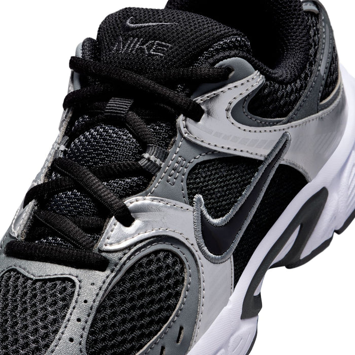 Nike youth sneaker upper close-up with black laces, silver overlays, and swoosh logo
