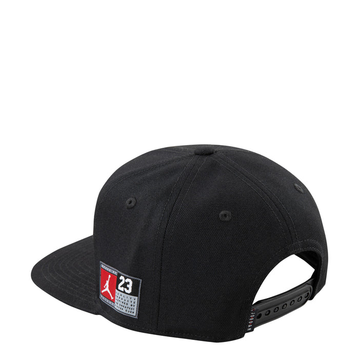 Black youth snapback cap with red-and-white side logo patch and flat brim